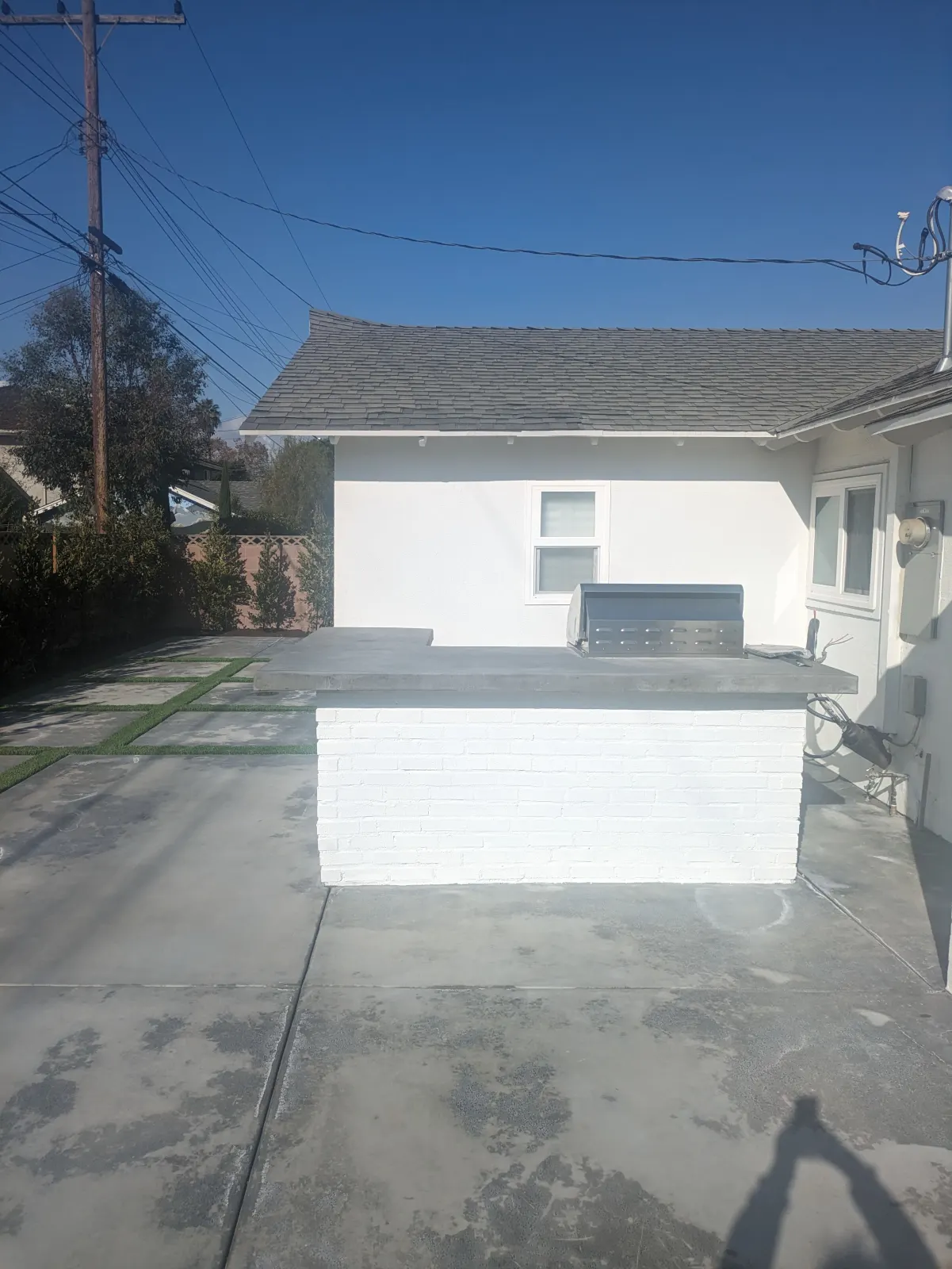 A concrete driveway or side-yard path with a white painted wall and home siding in the background.