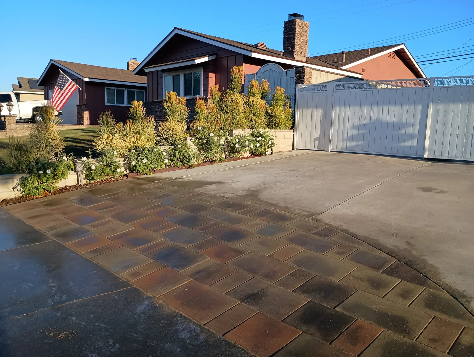 Driveway layout showcasing a section of reddish-brown interlocking stone pavers adjacent to solid concrete in front of a white fence.