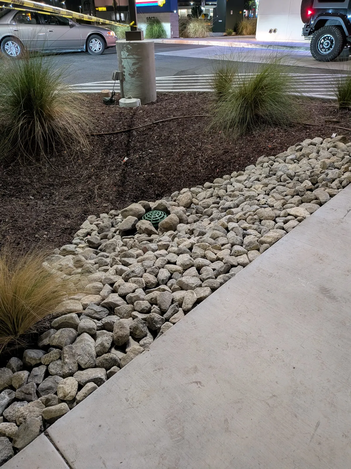 A detailed landscaping bed with a river rock dry stream, dark mulch, and ornamental grass clumps next to concrete.