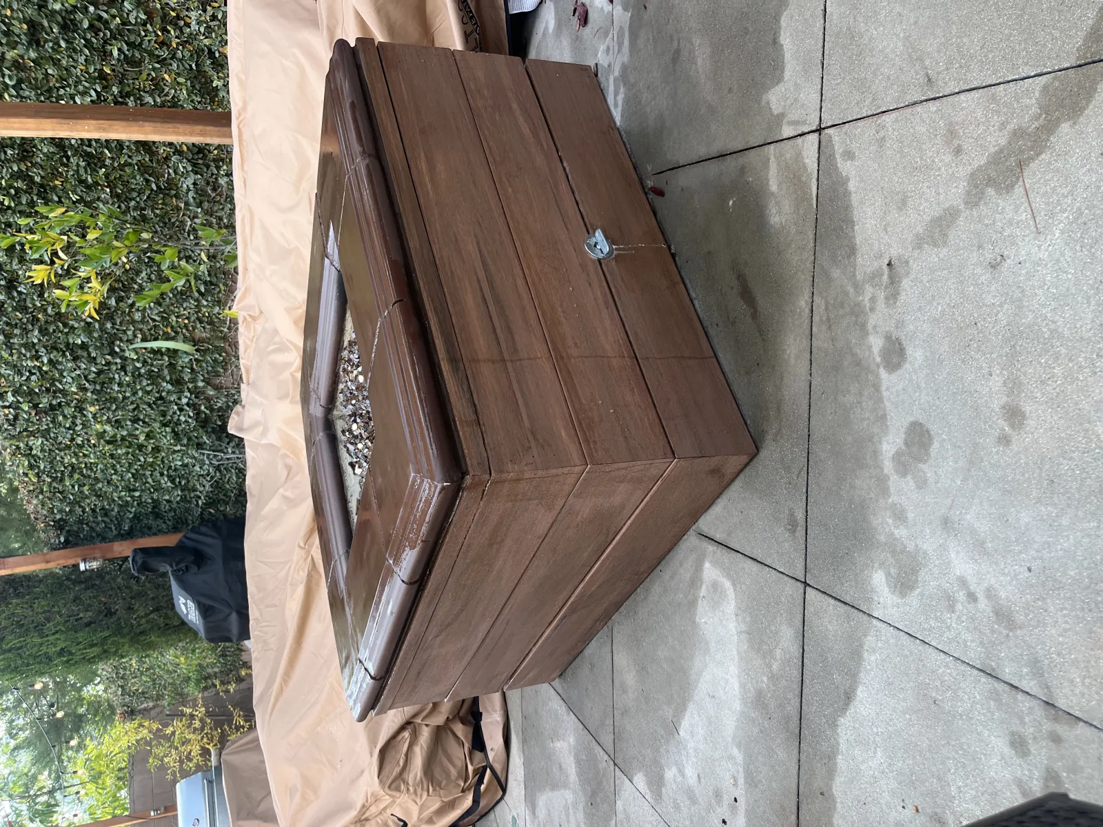 A close-up view of a stained wooden chest sitting on light grey stone patio pavers.